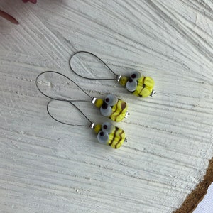 Könnte beinhalten: Drei gelbe und schwarze bienenförmige Glasperlen-Maschenmarkierer mit silbernen Drahtschlaufen.