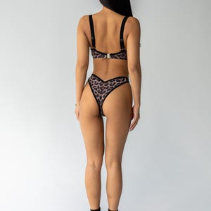 May include: Leopard print lingerie set featuring a bra with adjustable straps and a matching high-waisted thong. The set has a black trim and a silver clasp. The lingerie is made of a soft, patterned fabric.