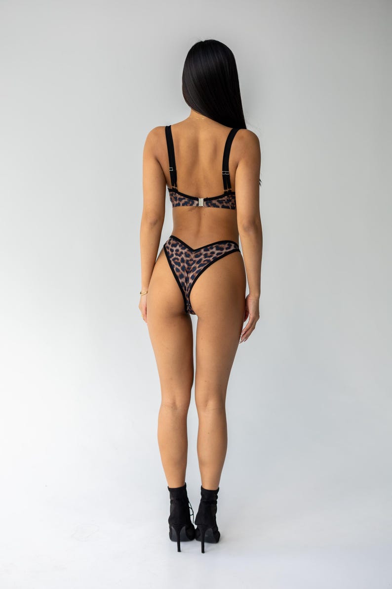 May include: Leopard print lingerie set featuring a bra with adjustable straps and a matching high-waisted thong. The set has a black trim and a silver clasp. The lingerie is made of a soft, patterned fabric.