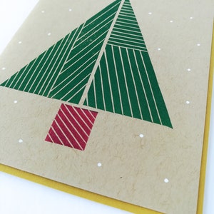 Op de afbeelding: Een kerstkaart met een geometrisch kerstboomontwerp in groen en rood op een bruine achtergrond met witte stippen.