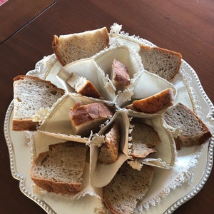 Może przedstawiać: Biały koszyk na chleb z tkaniny z srebrną obwódką, wypełniony kromkami brązowego chleba.