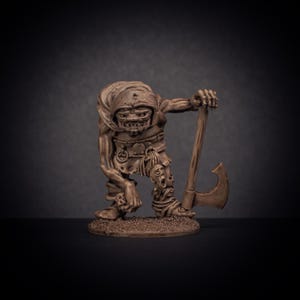 May include: A brown painted miniature figure of a goblin holding an axe. The goblin is wearing a hooded cloak and has a fierce expression on its face.