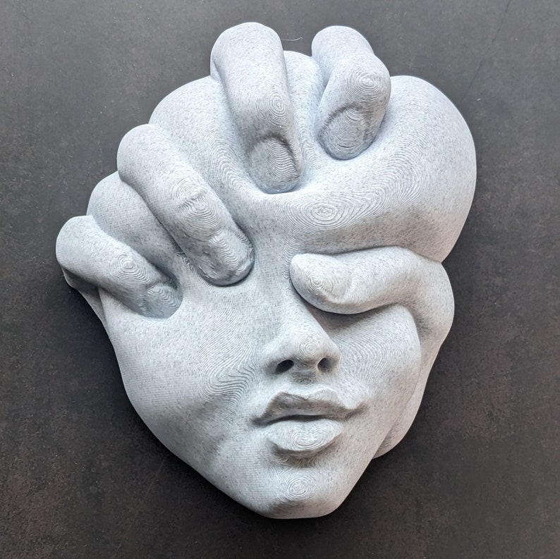 May include: A gray sculpture of a human face with hands covering the eyes and part of the face. The sculpture has a textured surface and is set against a dark background. The artwork is a unique piece of home decor.