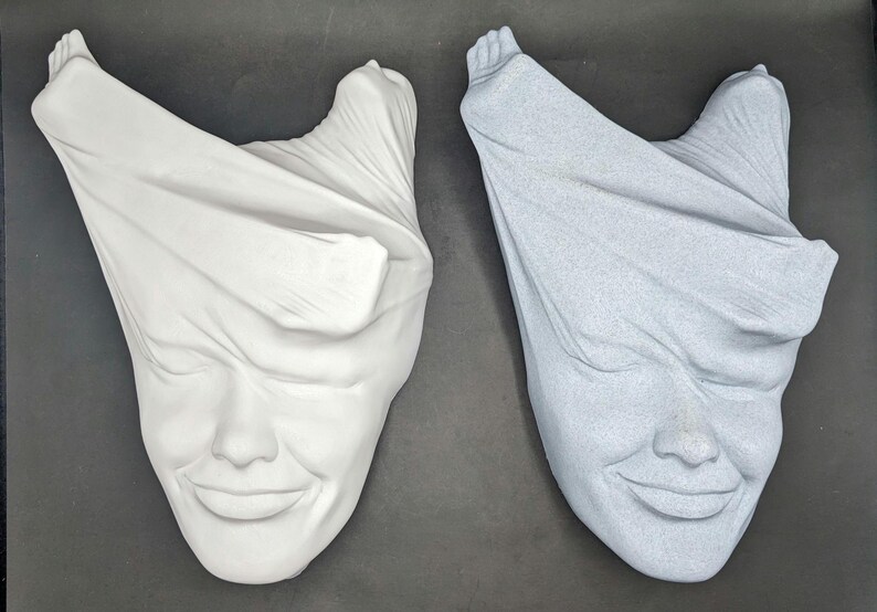 May include: Two white plaster sculptures of faces with fabric draped over them. One sculpture is white and the other is light blue.