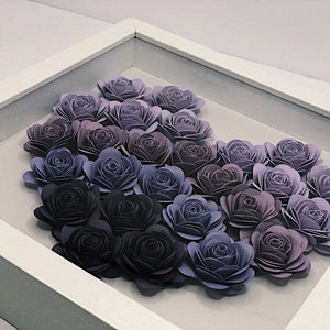 May include: A framed artwork featuring a gradient of purple paper flowers arranged in a heart shape. The flowers are made of layered paper and range in color from light lavender to dark purple.