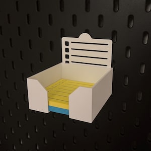 Könnte beinhalten: Weißer, wandmontierter Organizer aus Kunststoff mit einer Checkliste und einem Spender für Haftnotizen. Der Spender enthält gelbe, blaue und weiße Haftnotizen.