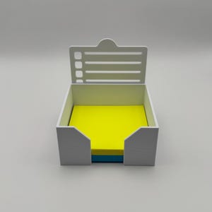 Könnte beinhalten: Weißer Plastik-Schreibtisch-Organizer mit einem Stapel gelber, blauer und grüner Haftnotizen im Inneren. Der Organizer hat einen aufklappbaren Deckel mit einer Checkliste.