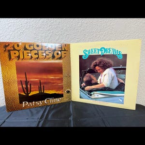 May include: Two vintage vinyl record albums. One album cover features the text "20 Golden Pieces Of Patsy Cline" with a desert landscape. The other album cover has the text "Sweet Dreams" with a couple in a car.