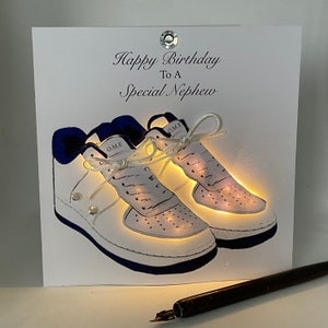 May include: A white card with a blue border and a white and blue illustration of two sneakers with the text "Happy Birthday To A Special Nephew" on the front.