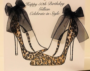 Op de afbeelding: Een witte kaart met zwarte tekst die "Happy 50th Birthday Gillian Celebrate in Style" luidt. De kaart toont een tekening van twee luipaardprint hoge hakken met zwarte strikken.