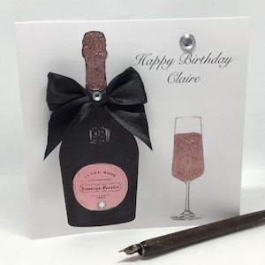 May include: A pink and black birthday card featuring a champagne bottle and glass. The bottle is decorated with a black bow and the text "Happy Birthday Claire".