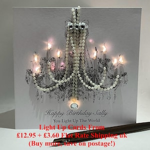 May include: A white birthday card with a black and white chandelier design, adorned with pearl detailing and small lights. The card's text reads "Happy Birthday Sally, You Light Up The World".
