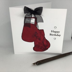 Może przedstawiać: Biała kartka z czerwonym bokserskim rękawem wiszącym na czarnej wstążce. Na kartce widnieje napis "Have a Great Day" i "Happy Birthday".