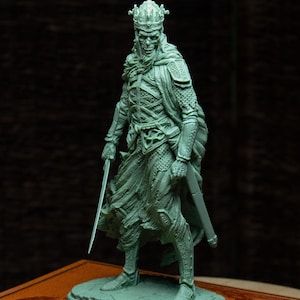 Può includere: Una statuetta in miniatura dipinta di verde di un re scheletrico con una corona e un'armatura, che tiene una spada. La statuetta è in piedi su una base di pietra.