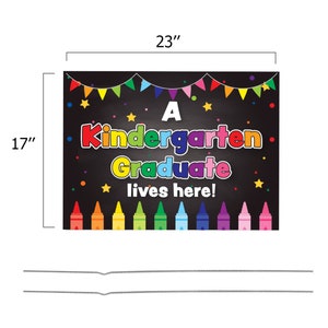 May include: A black chalkboard sign with the text "A Kindergarten Graduate lives here!" in colorful letters. The sign is decorated with colorful crayons, stars, and a string of flags.