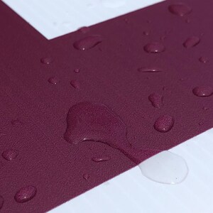 May include: Close-up of a deep burgundy surface with water droplets. The surface is textured and the droplets are round and clear.