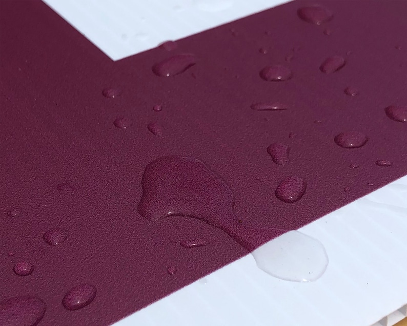 May include: Close-up of a deep burgundy surface with water droplets. The surface is textured and the droplets are round and clear.