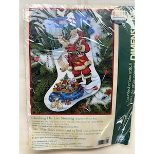 May include: A Dimensions counted cross stitch kit titled Checking His List Stocking. The packaging features an illustration of Santa Claus holding a list, standing above a blue stocking filled with toys, set against a pine tree background.