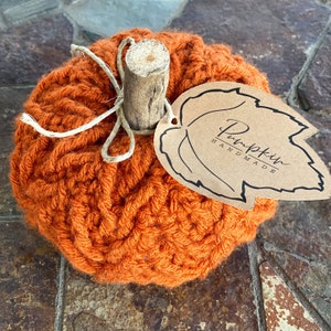 May include: A crocheted orange pumpkin with a twig stem and a brown paper tag that says "Pumpkin Handmade".