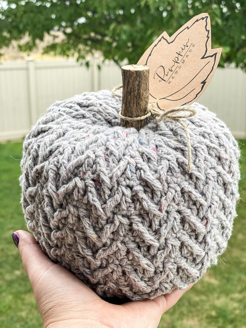 May include: A gray crocheted pumpkin with a brown twig stem and a brown paper tag that says "Pumpkin Handmade".