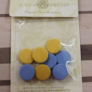 May include: A package of eight yellow and blue foam buttons for paper crafts. The package is labeled "Anna Griffin Elegant Embellishments" and "8 Button Embellishments for Decorating Your Papercrafts ©2006 Anna Griffin Inc."