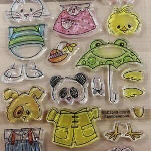 May include: Clear acrylic stamps featuring various cartoon animal designs, including a bunny, tiger, bear, chick, frog, panda, dog, and sheep. Other stamps include a skirt, hat, umbrella, overalls, raincoat, boots, and chicken feet. The text "SSC1240 ©2015 Stampendous" is visible.