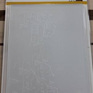 May include: A clear, rectangular stamp with a detailed embossed design of a village scene. The stamp is packaged in a clear plastic sleeve. The top of the package has the text "SIMON SAYS STAMP!" and a Boston Terrier illustration.