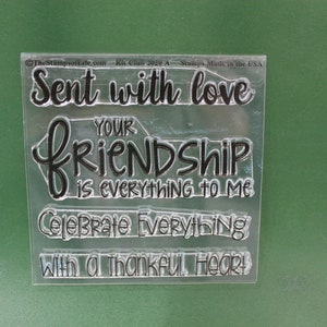 May include: Clear acrylic stamp set with four phrases: "Sent with love", "Your friendship is everything to me", "Celebrate everything", and "With a thankful heart".