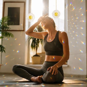 May include: Three circular suncatchers with intricate gold-toned wire spokes and central yellow crystals hang from thin strings, casting vibrant rainbow light refractions across the room while reflecting sunlight through the window.