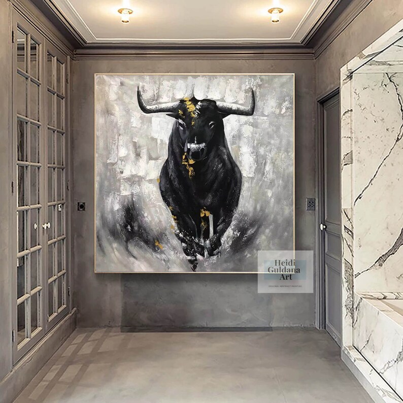 May include: Large framed abstract painting of a black bull charging forward. The bull has long horns and gold accents against a gray and white textured background. The artwork is displayed in a modern hallway.