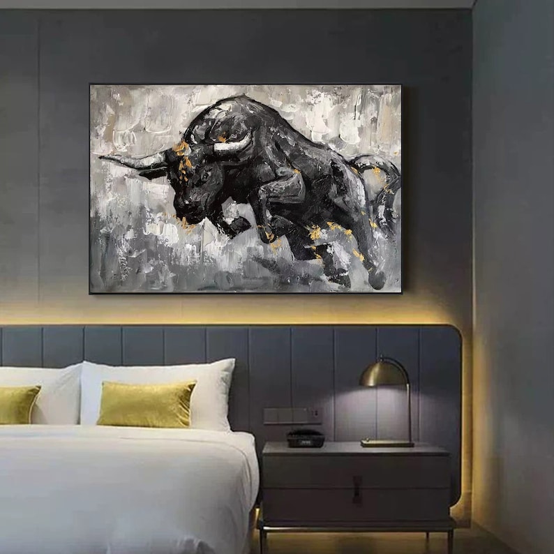 May include: A black and white abstract painting of a bull charging forward. The bull is painted in a dark shade of black with gold accents. The background is a light gray with white brushstrokes.