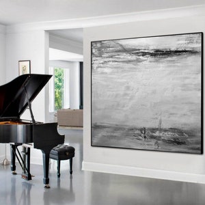 Op de afbeelding: Een abstract zwart-wit schilderij met een horizontale compositie. Het schilderij heeft een textuur, gelaagd effect met tinten grijs en wit. Het schilderij is ingelijst in een zwart frame en hangt aan een witte muur.