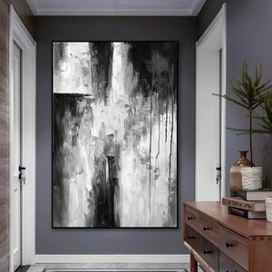 Puede incluir: Pintura abstracta en blanco y negro sobre lienzo con pinceladas gruesas y goteos de pintura. La pintura est&aacute; colgada en una pared gris en un pasillo.