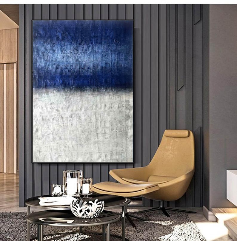 Puede incluir: Pintura abstracta con un esquema de color azul y blanco. La pintura est&aacute; colgada en una pared en un ambiente de sala de estar moderna. La pintura est&aacute; enmarcada y tiene una superficie texturizada.