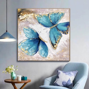 May include: A painting of two blue butterflies with gold accents on a white background. The butterflies are painted in a realistic style and have a textured appearance.