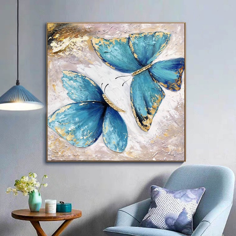 May include: A painting of two blue butterflies with gold accents on a white background. The butterflies are painted in a realistic style and have a textured appearance.
