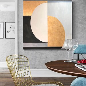 May include: Abstract geometric painting with a black, white, gold, and gray color scheme. The painting features a large circle with a smaller circle inside, and a series of geometric shapes.