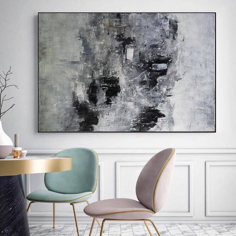 May include: Abstract painting with black and grey brushstrokes on a white canvas. The painting is framed in a black frame and is hanging on a white wall.