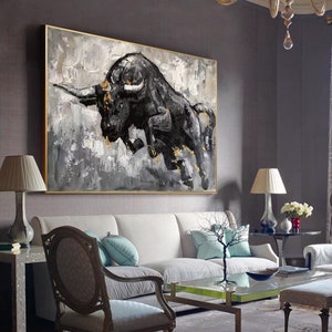 May include: A black and white abstract painting of a bull charging forward. The bull is painted in a bold, expressive style with gold accents. The background is a textured gray and white.