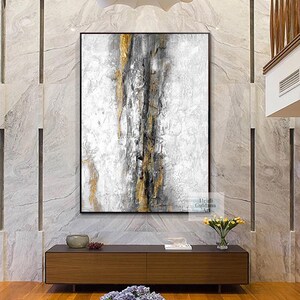 May include: Abstract painting with gold and gray accents on a white background. The painting is framed in black and is hanging on a wall above a wooden console table.