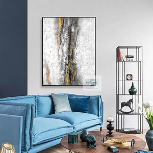 May include: Abstract painting with a white background and gold and gray accents. The painting is hanging on a white wall above a blue sofa.