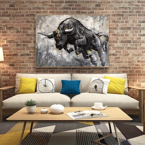 May include: A black and white painting of a bull charging, with gold accents. The painting is framed and hanging on a brick wall above a couch.