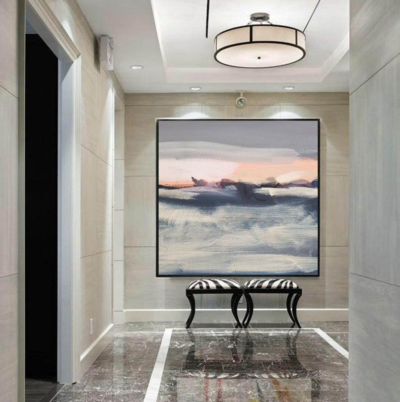 May include: A large abstract painting in shades of gray, blue, and pink hangs on a wall in a hallway. The painting is framed in black and is centered above two black and white zebra-striped stools.