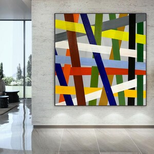 May include: Abstract painting with a geometric design featuring intersecting lines in various colors, including red, yellow, blue, green, white, and brown. The lines are arranged in a chaotic pattern on a gray background.