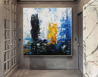 May include: Abstract painting with bold strokes of black, white, blue, and yellow paint. The painting is framed and hanging on a gray wall in a hallway.
