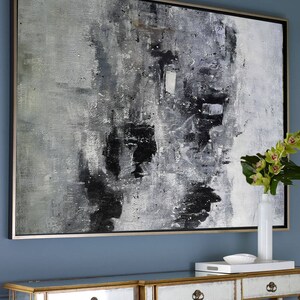 May include: Abstract black and white painting in a silver frame hanging on a blue wall above a mirrored console table with gold accents.