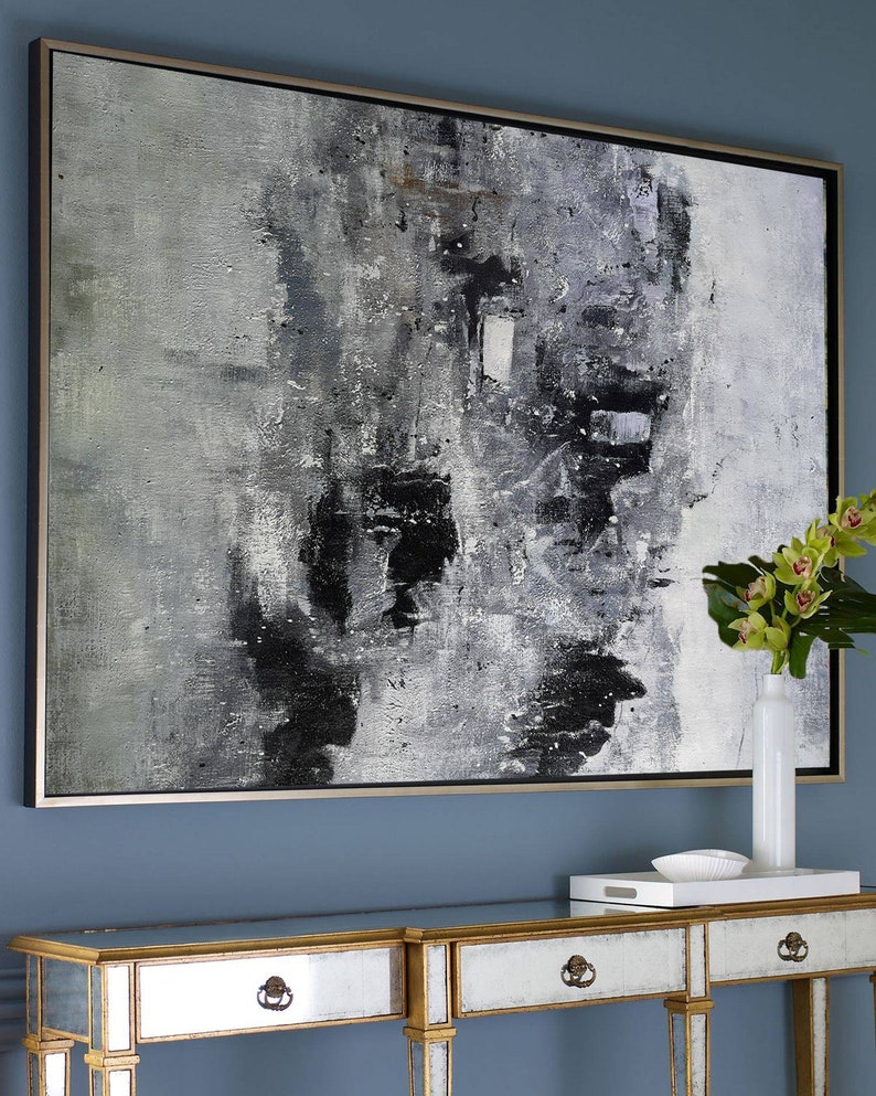 May include: Abstract black and white painting in a silver frame hanging on a blue wall above a mirrored console table with gold accents.