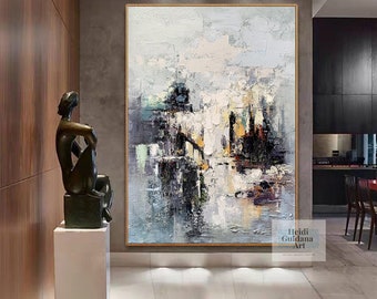 May include: Abstract painting with a cityscape theme. The painting features a mix of blues, grays, and whites with hints of yellow and orange. The painting is framed in a gold frame and is hanging on a wall in a modern home.