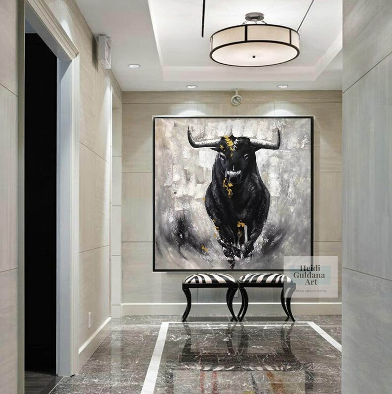 May include: Large black and white bull painting with gold accents. The artwork is displayed in a hallway with a black frame. The painting is above a black and white striped bench. The artist's name is in the bottom right corner.