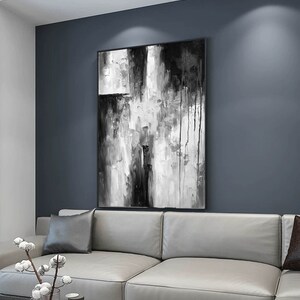 Puede incluir: Una pintura abstracta en blanco y negro con un sof&aacute; gris y una mesa de caf&eacute; de m&aacute;rmol en primer plano. La pintura est&aacute; colgada en una pared gris.